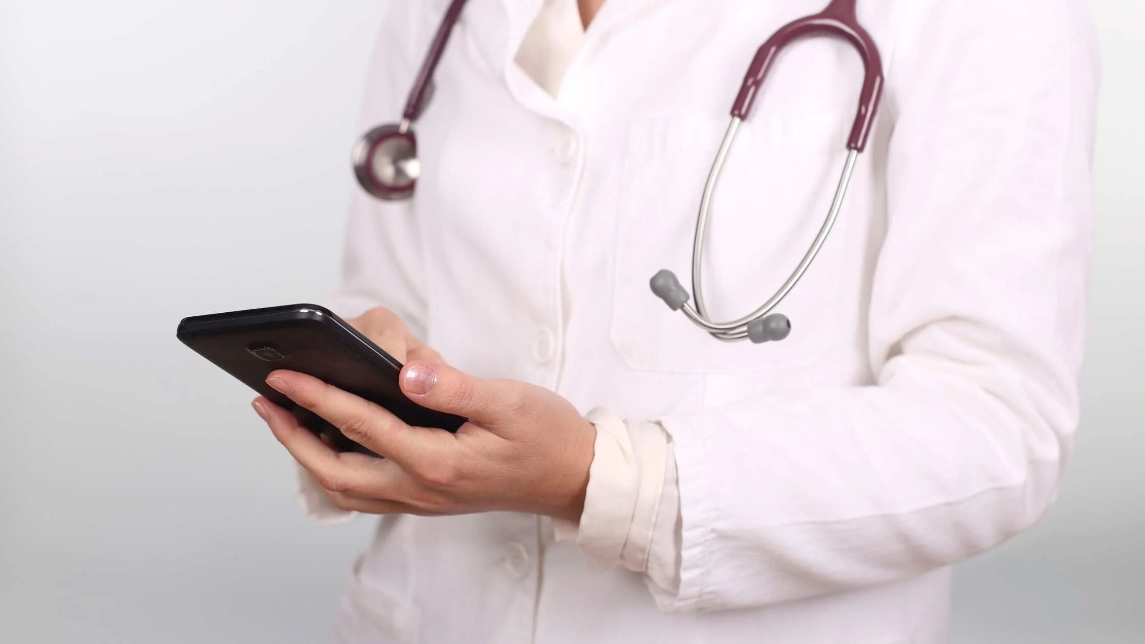 Close up of doctor wearing lab coat and stethoscope and using mobile phone